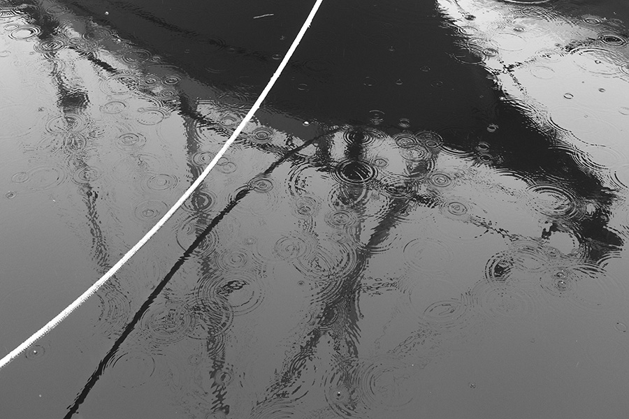 Black and White Photo of Reflection of a Sailboat in the Water with Raindrop Circles.